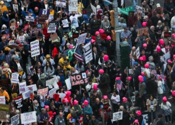 People protest in Times Square against Trump's policies, holding various signs including "NO KINGS" and "MAKE AMERICA ANTIFA AGAIN."