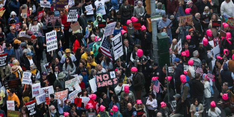 People protest in Times Square against Trump's policies, holding various signs including "NO KINGS" and "MAKE AMERICA ANTIFA AGAIN."