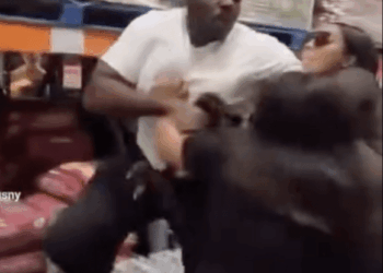 Man in white shirt punching a woman, with another woman on the ground, in what appears to be a Costco aisle.