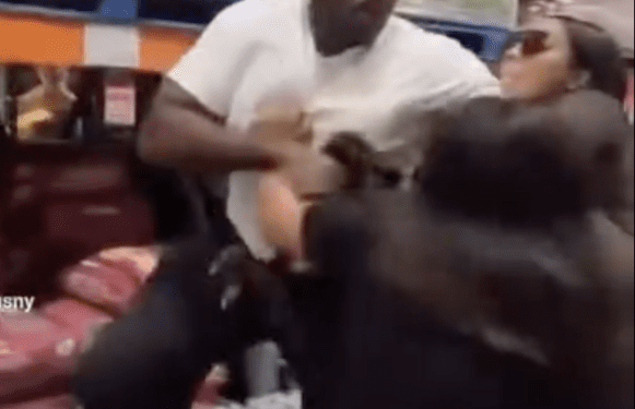 Man in white shirt punching a woman, with another woman on the ground, in what appears to be a Costco aisle.