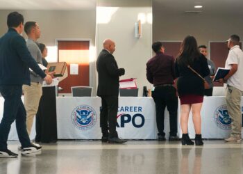 Several people dressed in business attire line up in front of a booth at a hiring event.