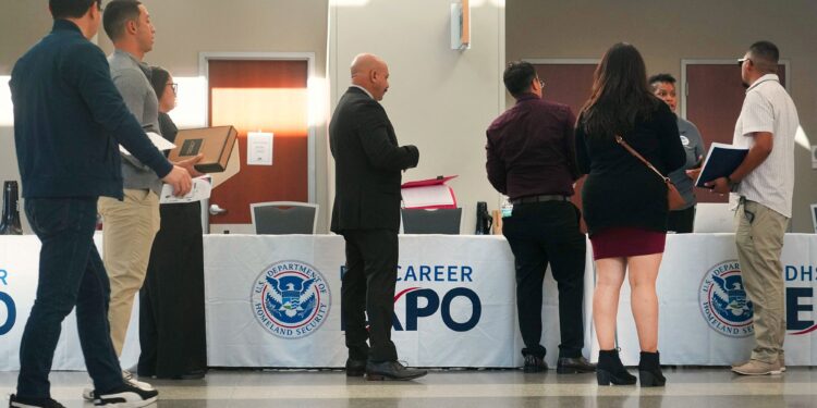 Several people dressed in business attire line up in front of a booth at a hiring event.