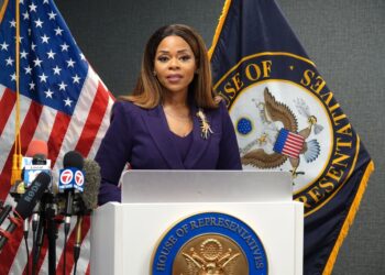 Congresswoman Sheila Cherfilus-McCormick speaks at a news conference, flanked by American and House of Representatives flags.