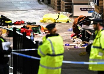 Paramedics' medical equipment, including bags and yellow protective gear, on the ground behind a police cordon at Huntingdon Station after a stabbing on a train.