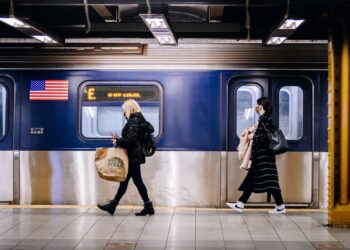 People wearing protective masks walk past a subway train.