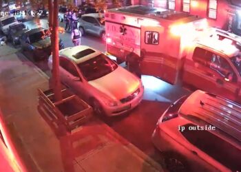 An ambulance and police cars on a street with officers and people standing near the vehicles.