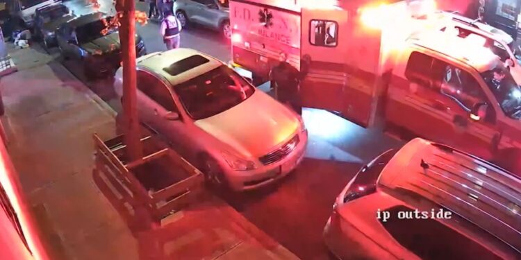 An ambulance and police cars on a street with officers and people standing near the vehicles.