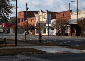 A view of Lumpkin's downtown, which is composed of small brick buildings, including three red ones, two white ones and a pale blue one. All of the parking spaces in front of the buildings are empty.