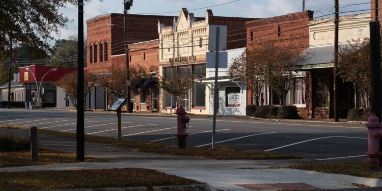 A view of Lumpkin's downtown, which is composed of small brick buildings, including three red ones, two white ones and a pale blue one. All of the parking spaces in front of the buildings are empty.
