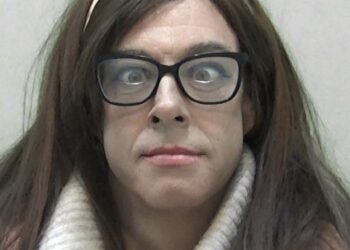 Natalie Wolf, a convicted child sex offender, wearing glasses, a wig, and a cream-colored turtleneck.